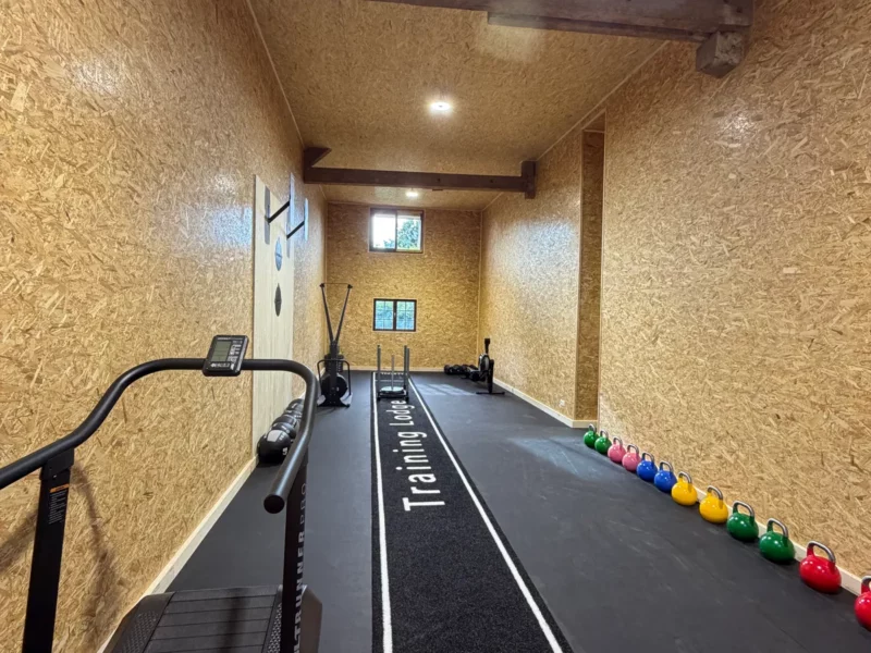 La salle d'entraînement du Training Lodge : tapis central, mur de kettlebells et AssaultRunner